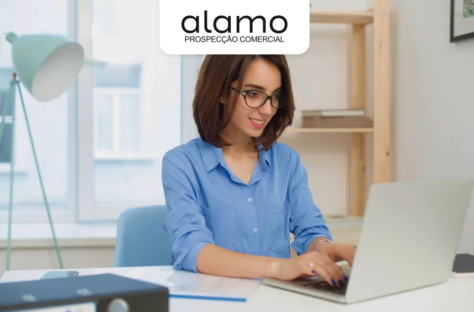 Mulher usando óculos trabalhando em notebook em ambiente de escritório claro, com o logotipo da Álamo Prospecção Comercial no topo da imagem.